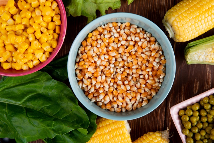 close-up view of bowl full of corn seeds with spinach cooked corn seeds green peas on wooden background